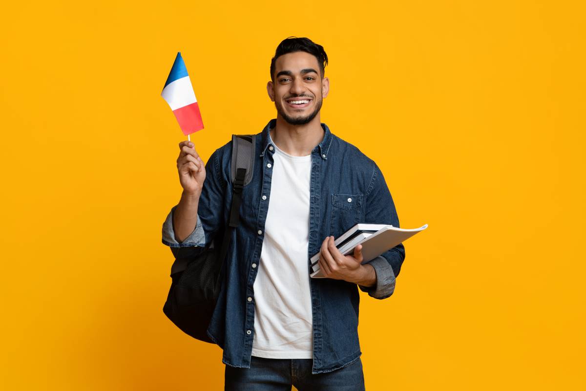 Un homme avec le drapeau français tenant des livres et un sac à dos sur un fond jaune. Etudier en France comme Tunisienne.