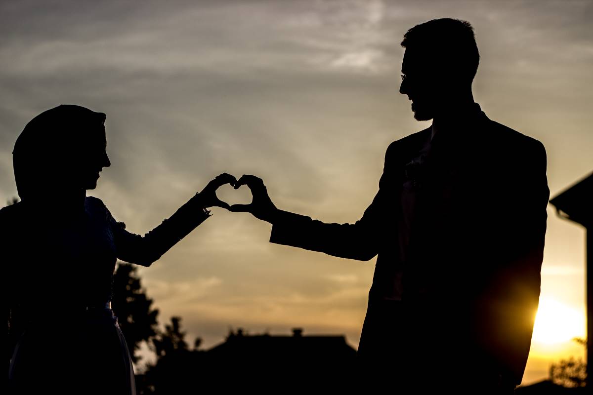 Silhouette d'un couple se tenant face à face, formant un cœur avec leurs mains jointes contre un coucher de soleil. La scène évoque l'union et la célébration de l'amour, pertinent pour les couples cherchant à valider leur mariage célébré à l'étranger en Tunisie